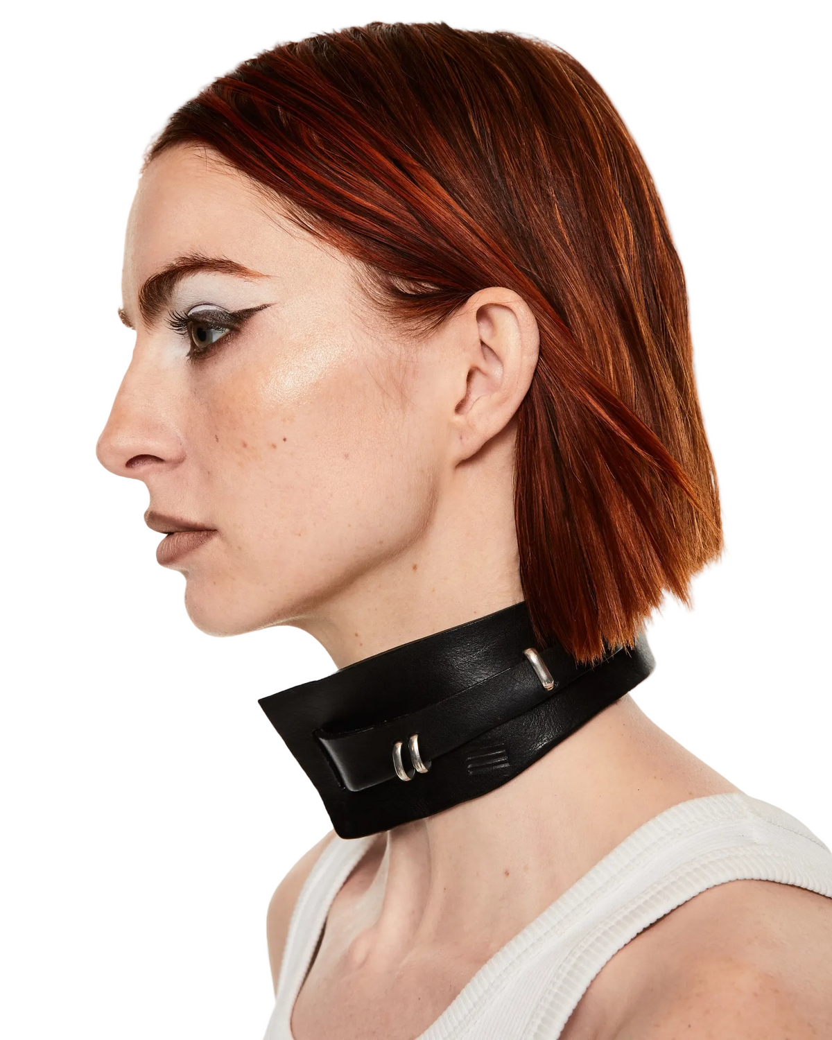 A side-profile portrait of a woman with short auburn hair wearing a black leather choker collar with silver metal hardware, set against a plain white background.