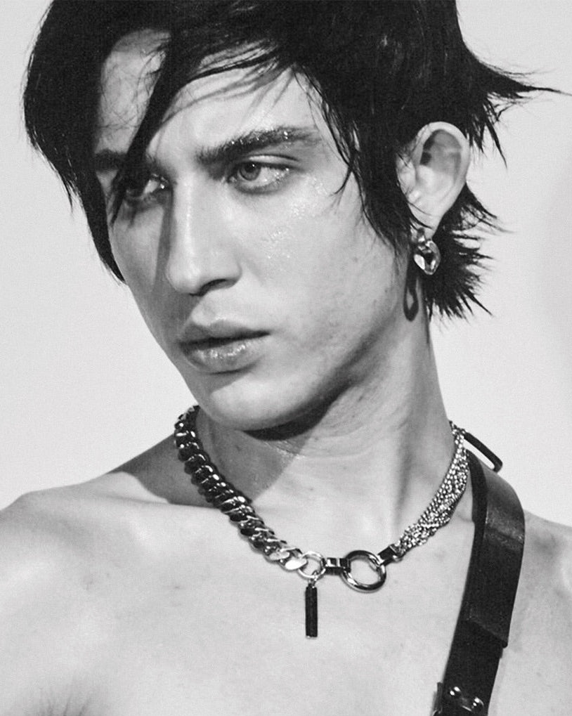 Black and white portrait of a shirtless person with a necklace and bag strap over shoulder.