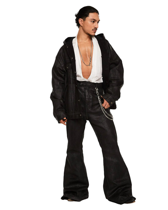 A model wearing a black leather jacket, black flared jeans, and a white open-collar shirt, standing against a plain white studio background.
